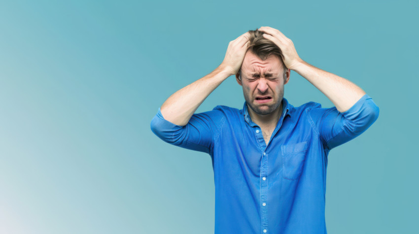 A man in a blue shirt holds his head with both hands illustrating healthcare and headache concept