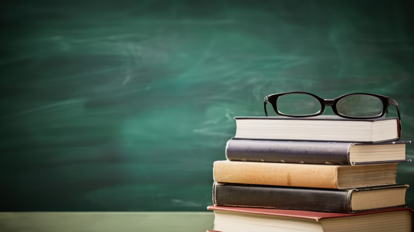 Books stacked neatly with glasses and pencils on a classroom chalkboard celebrating teachers day educational tools