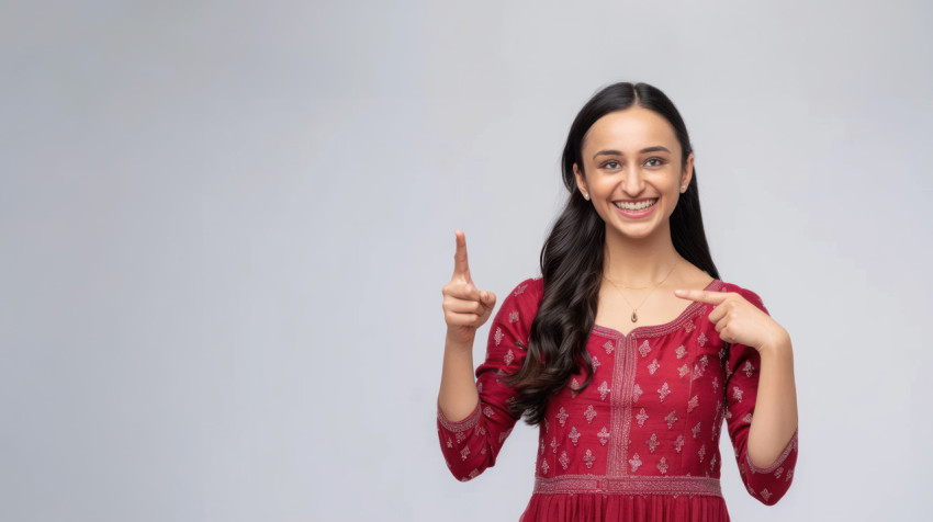 Beautiful indian woman in a red dress smiling and pointing to the right side with her finger standing against a white background