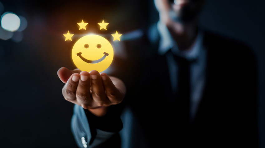 Businessman holding yellow smiley face icon with four stars on dark background representing customer satisfaction