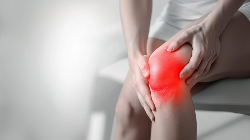 A man holding his knee in pain with visible redness against a mostly white background