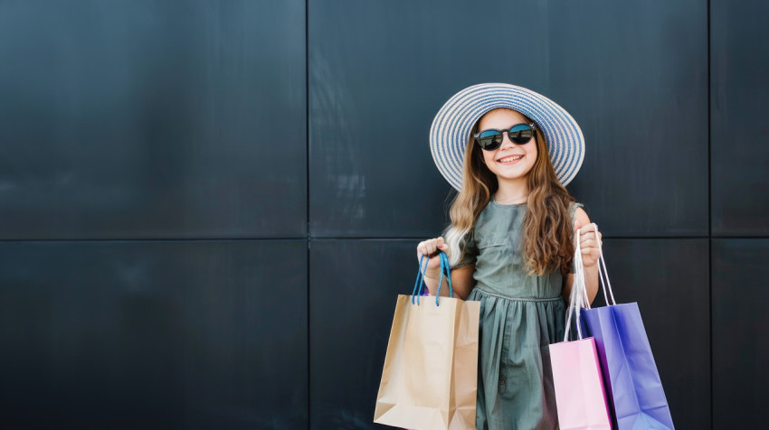 A young woman in sunglasses hat holds shopping bags against black background