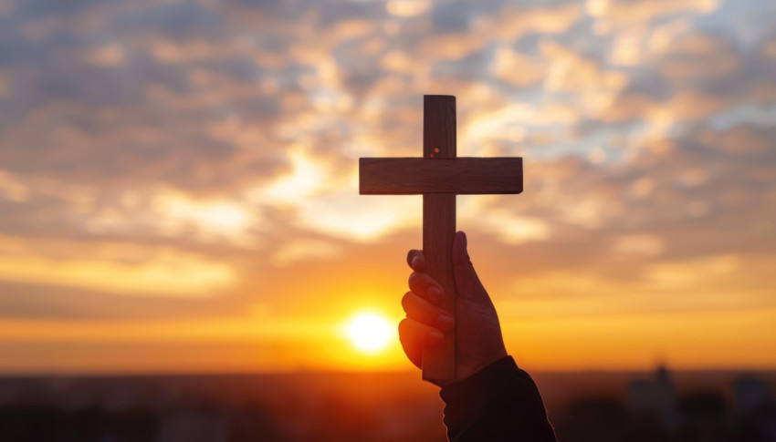 Hand holding cross in silhouette against sunrise backdrop