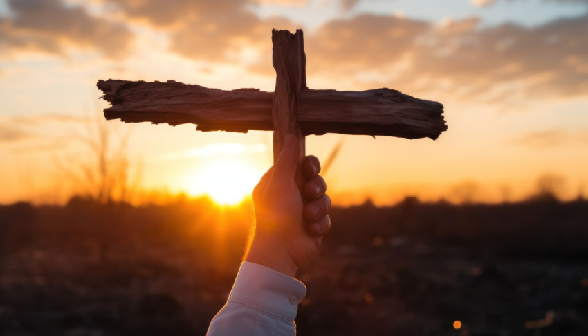 Hand holds cross against on sunrise