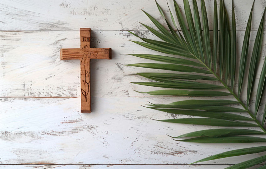 A wooden cross and palm leaf resting on a white table