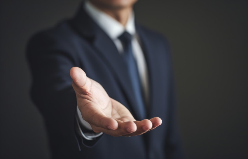 Businessman extends open hand against grey backdrop