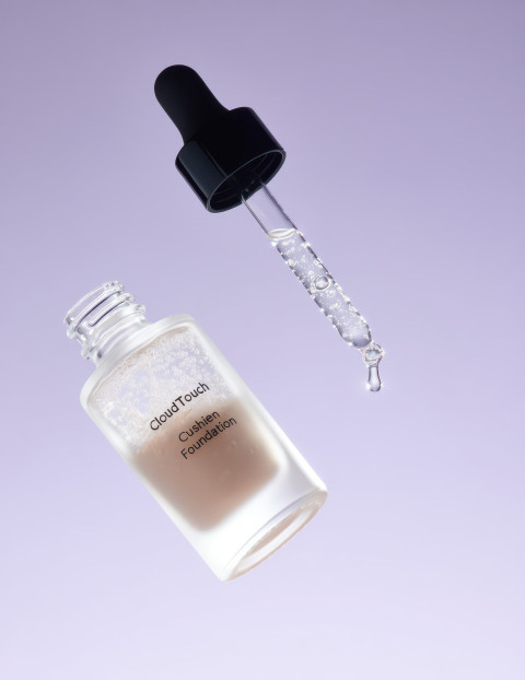 Glass serum foundation bottle with tiny bubbles and dropper dripping liquid under cool light on lavender background Glass serum foundation bottle with tiny bubbles and dropper dripping liquid under cool light on lavender background