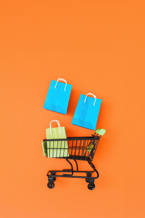 A black shopping cart with two colorful paper bags floating above an orange background