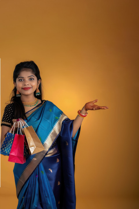 Indian woman in saree holding shopping bags and pointing at product against an isolated background