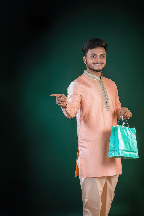 Attractive bangladeshi man in light peach colored kurta pants with blurred dark green background