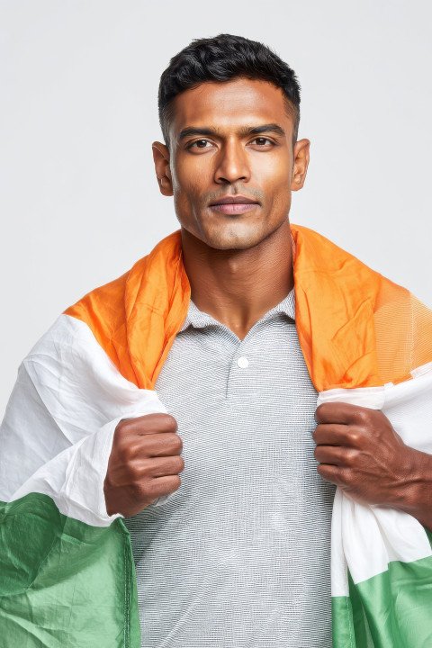Confident Indian man in grey polo holding unfurled flag across shoulders
