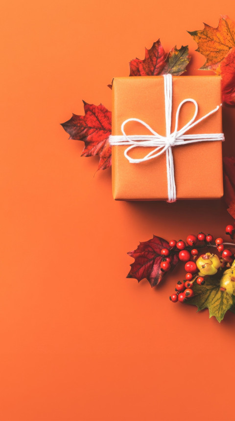 A gift box adorned with autumn leaves and berries on an orange background