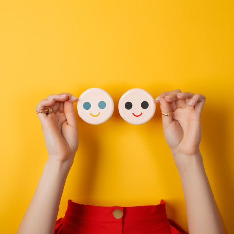 female hands holding four colored smiley stickers isolated on ye